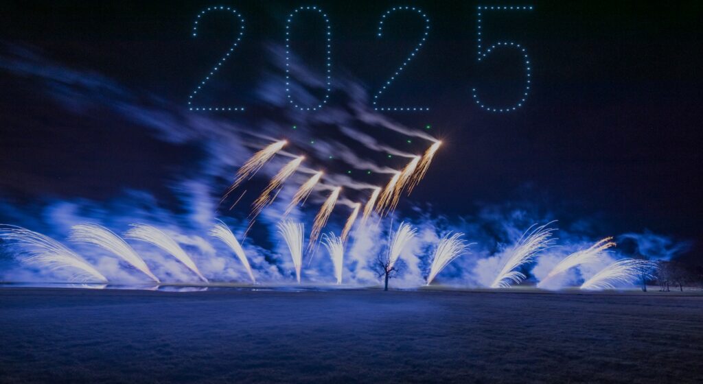 A mesmerizing fireworks and drone light show illuminates the night sky, with drones artfully forming "2025" above the field.