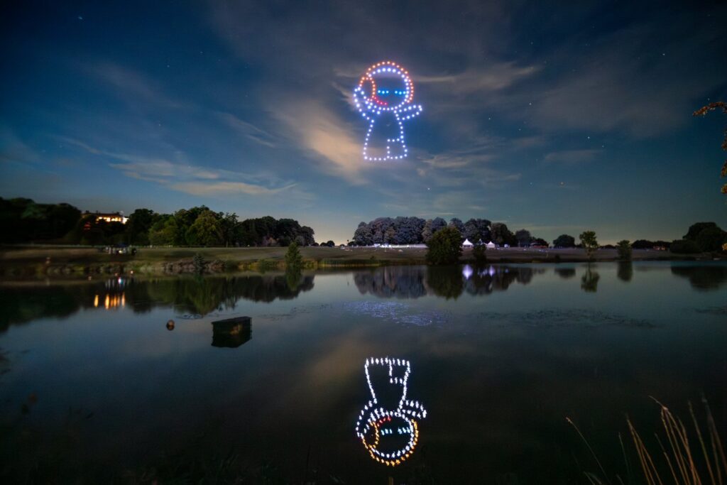 A drone light display forms a figure over a serene lake at night, with the figure's reflection visible in the water.