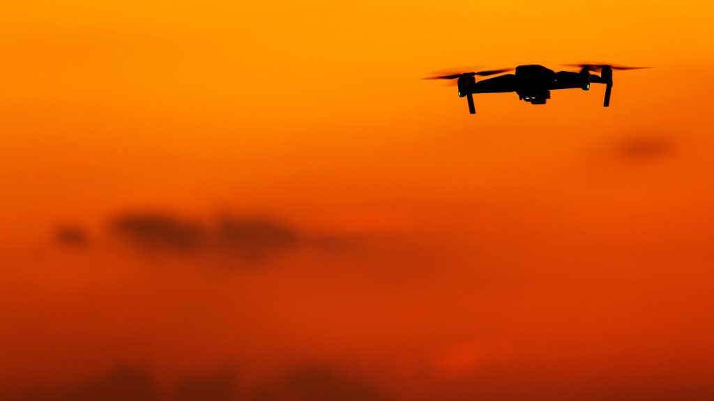 Silhouette of a drone performing in the Osmaston Park Wedding Drone Show against an orange sunset sky.