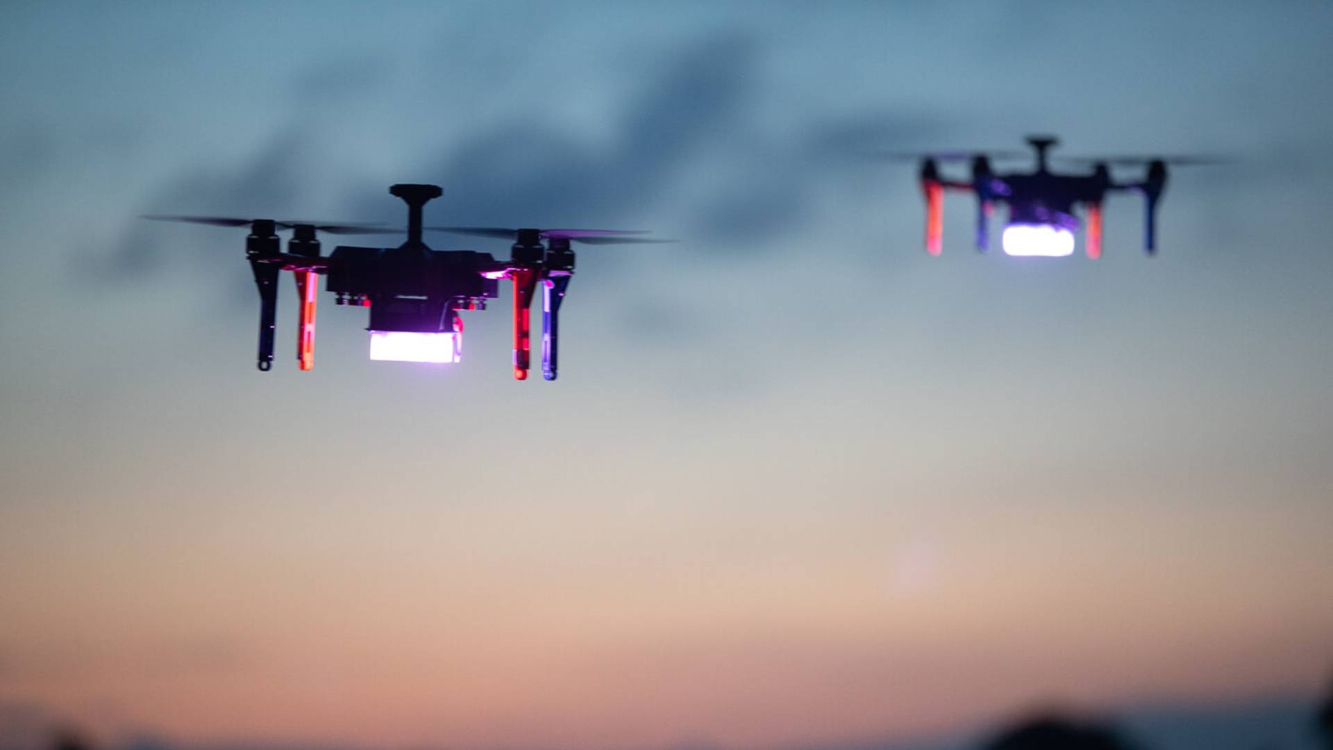 Two drones with glowing lights dance elegantly across the blurred evening sky, reminiscent of an enchanting Osmaston Park Wedding Drone Show.