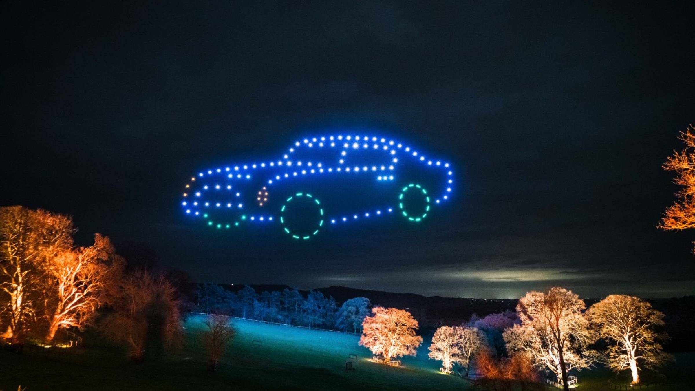 An enchanting drone light display of a car silhouette graces the night sky above an illuminated landscape, reminiscent of the stunning Osmaston Park Wedding Drone Show.