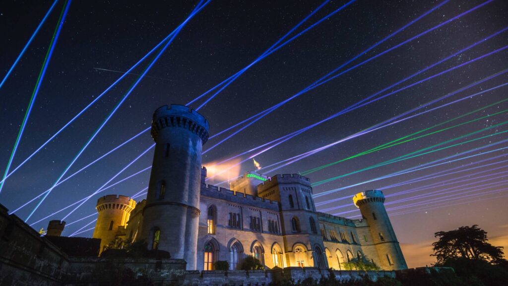 Amid a starry night sky, Osmaston Park comes alive with colorful laser beams crossing overhead, creating a magical backdrop for the wedding drone show.