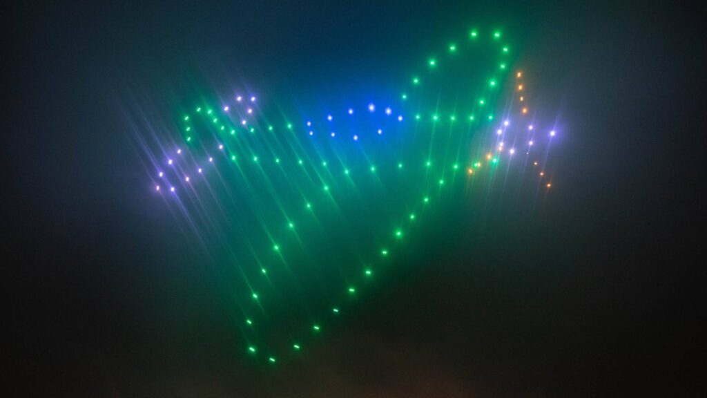 A vibrant Christmas drone light show transforms the night sky, forming a glowing airplane shape with colorful brilliance.