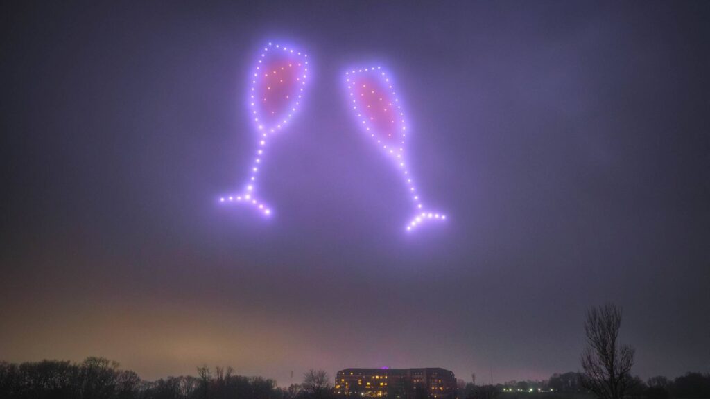 A mesmerizing drone light show illuminated the night sky, crafting two glowing champagne glasses above a building.