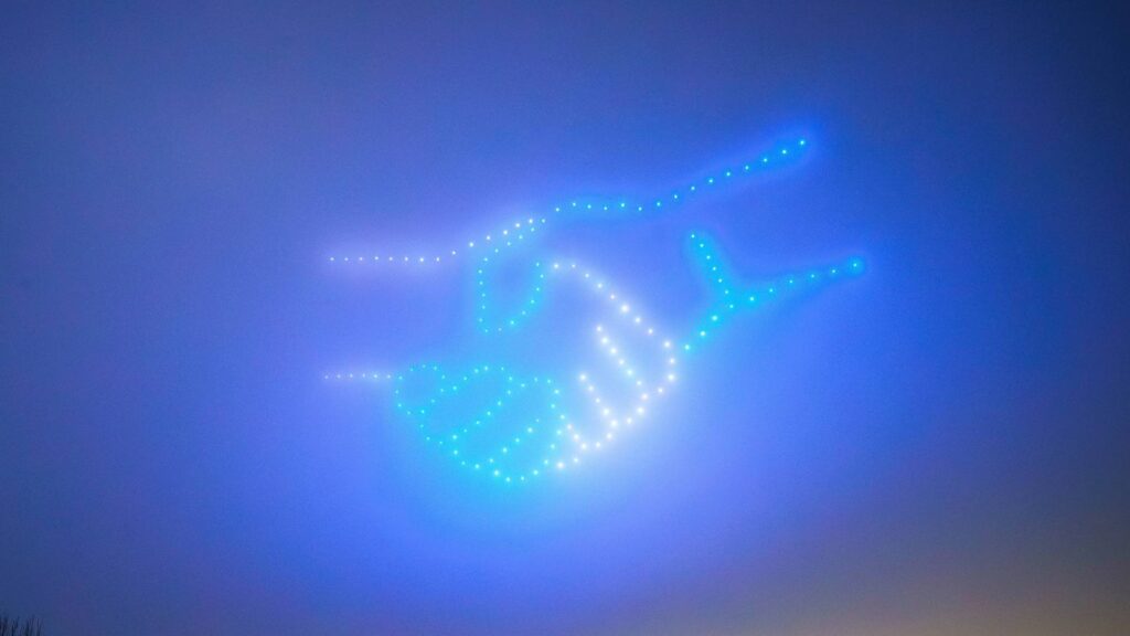 In a mesmerizing display, a drone light show paints the twilight sky with glowing designs, forming an intricate handshake that captivates all who gaze upward.