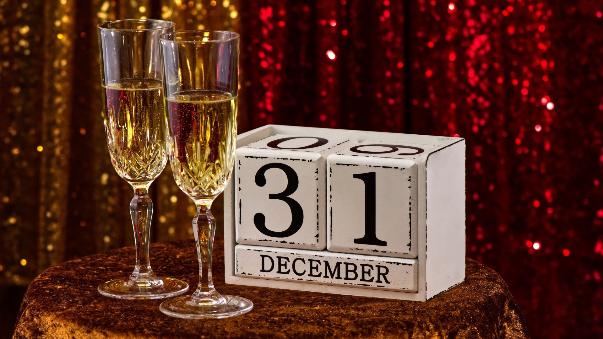 Two champagne glasses and a block calendar showing December 31 against a festive, glittery background.