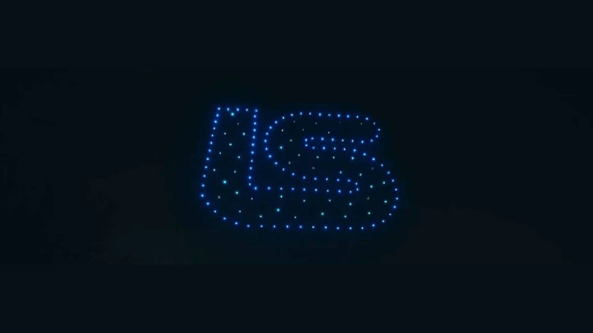 A drone light show features blue drones forming the letters "US" in the night sky against a dark background.