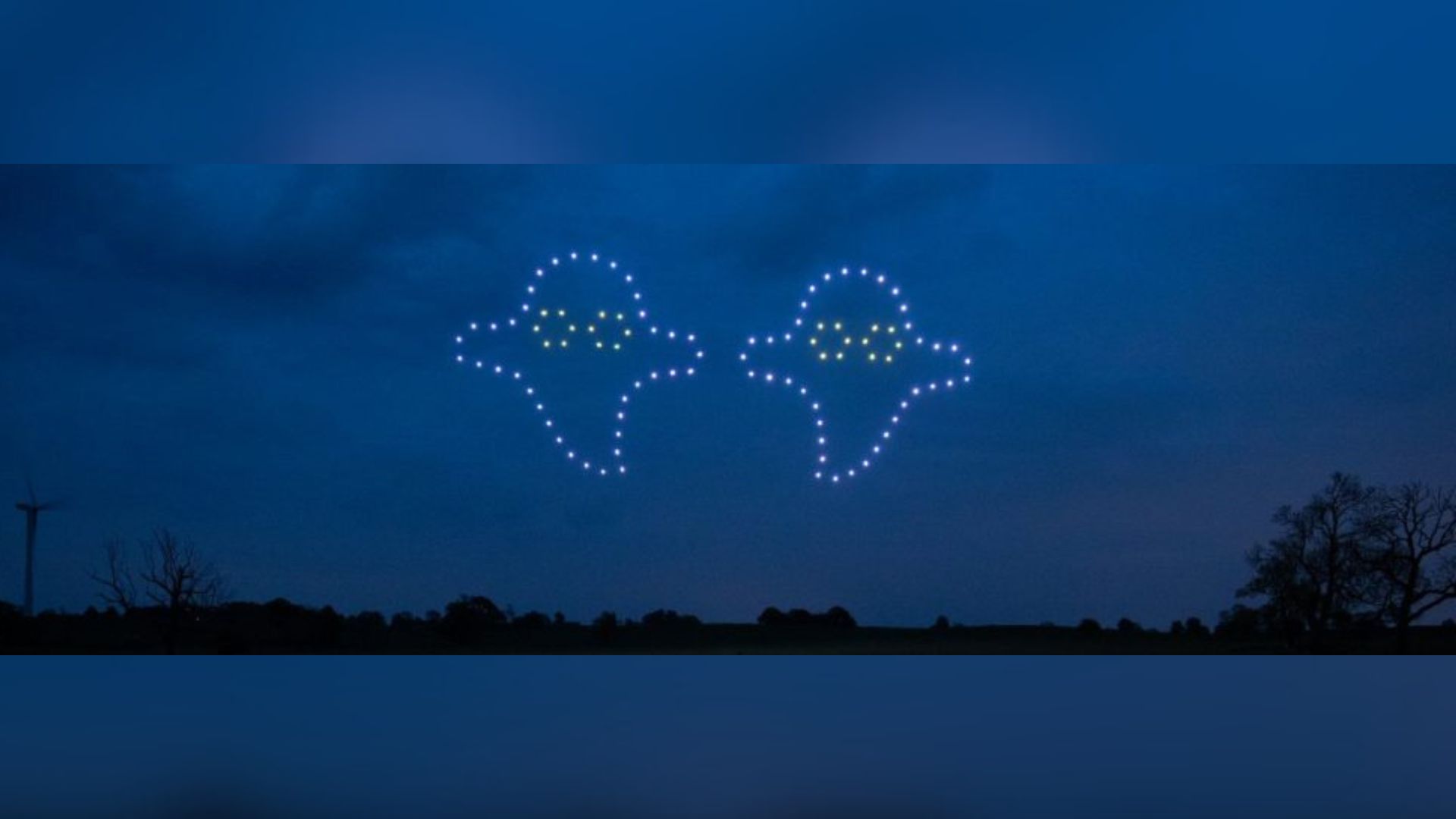 Two ghost shapes made of drone lights hover in the night sky over a dark landscape.