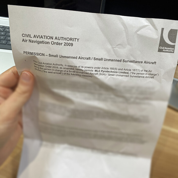 A hand holds a crumpled document titled "Civil Aviation Authority Permission – Small Unmanned Aircraft.